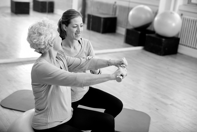 Senior woman lifts weight with help of instructor
