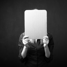 Woman holding empty cardboard in front of her face for facial masking