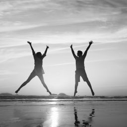 A man and woman jump into the air at the beach
