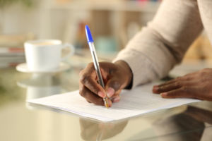 Close up of man's hands filling out form on a desk at home