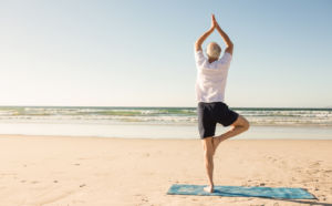 Senior man doing yoga on beach