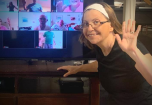 Woman waving to camera with video conference in background