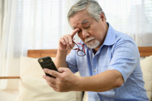 Portrait photo of senior Asian man has a eye long sighted problem trying to read message from smartphone