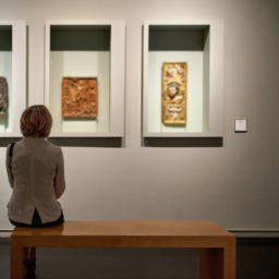 rear view of woman sitting in an art gallery in front of three pieces of art