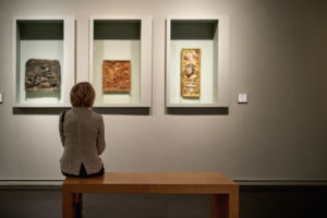 rear view of woman sitting in an art gallery in front of three pieces of art