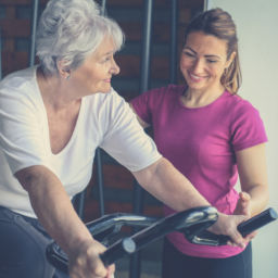 Senior woman exercising on stationary bikes in fitness class. Woman workout in gym. Senior with personal trainer.