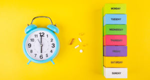 Alarm clock, pills and a multicolored weekly pill organizer