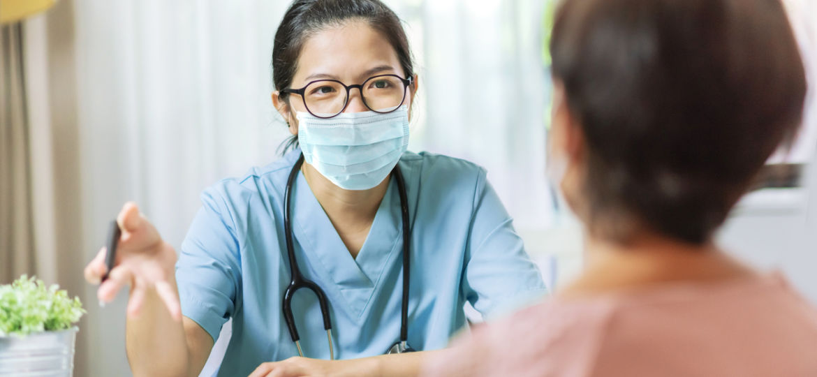 Young female Doctor in blue uniform and protective face mask giving advice to Senior female patient