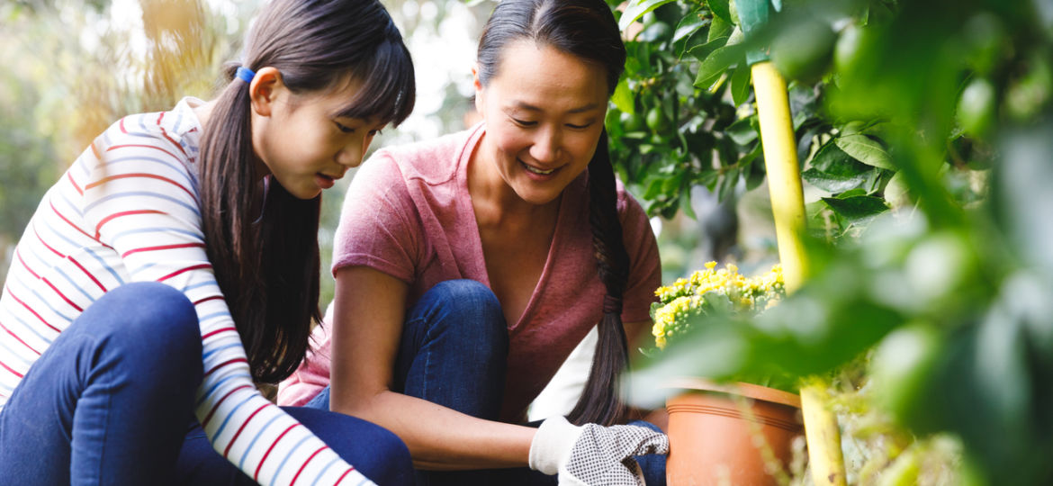 mother and daughter smiling, wearing gloves and working in garden