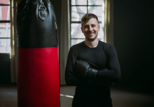 Male boxer smiles standing next to punching bag in gym