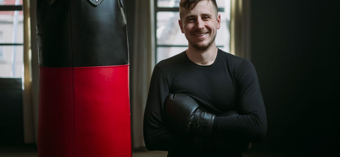 Male boxer smiles standing next to punching bag in gym