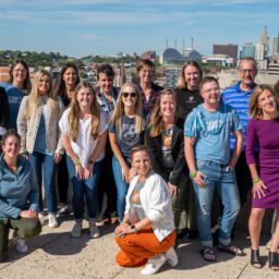 2022 HPC Leadership Conference Davis Phinney Foundation. The staff is in front of the Kansas City skyline. They are all smiling and staring into the sun.