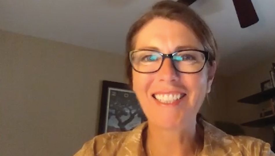 Parkinson's depression. Joanne hamilton is smiling and wearing glasses. She has brown hair and a yellow button-down. She is in front of a room with a fan.