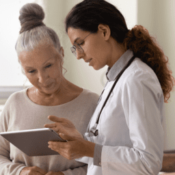 Tools. Two white women, one young and one a senior, look at an iPad. The senior woman has a white and grey bun and a white shirt. The younger one has a brown ponytail and a white lab coat.