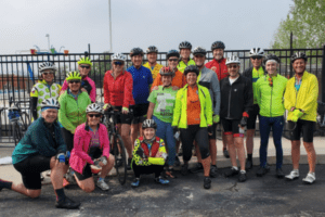 A team of bikers stands together, smiling. They are wearing shorts, neon colors, and helmets.