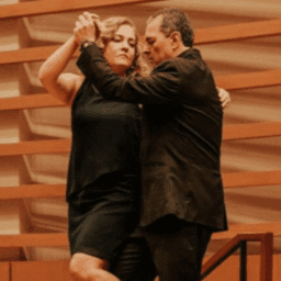 Jaime Robledo tango dances on a wooden stage. He and his partner are wearing all black. He has Parkinson's.