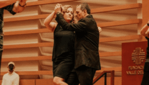 Jaime Robledo tango dances on a wooden stage. He and his partner are wearing all black. He has Parkinson's.
