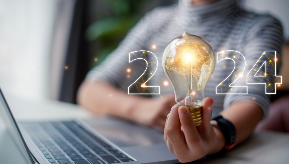 free a person holding a light bulb in front of a laptop with the number 2024 written in front of the blurry background. The 0 is the light bulb. There are lines and dots that are glowing gold throughout the picture. The lightbulb has a brain in it.