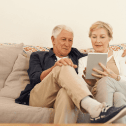 Two white seniors sitting on their couch looking at an iPad to find ways to gain independence.